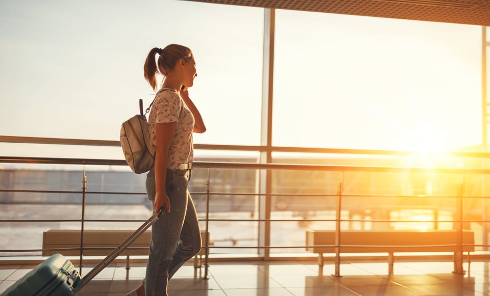 Young woman on phone in airport window with luggage